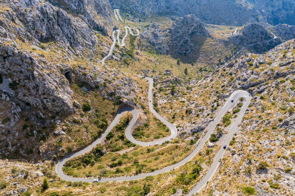 Winding asphalt mountain road with sharp curves and hairpin turns in rocky terrain, with vehicles and dry hillside vegetation, Landscape, Lifestyle, Sa Calobra, Mallorca, Spain.