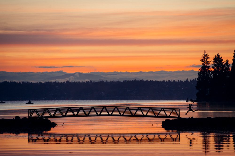 Silhouette of a person jumping from a dock over calm water at sunset, shington, Bainbridge Island, WA, USA.