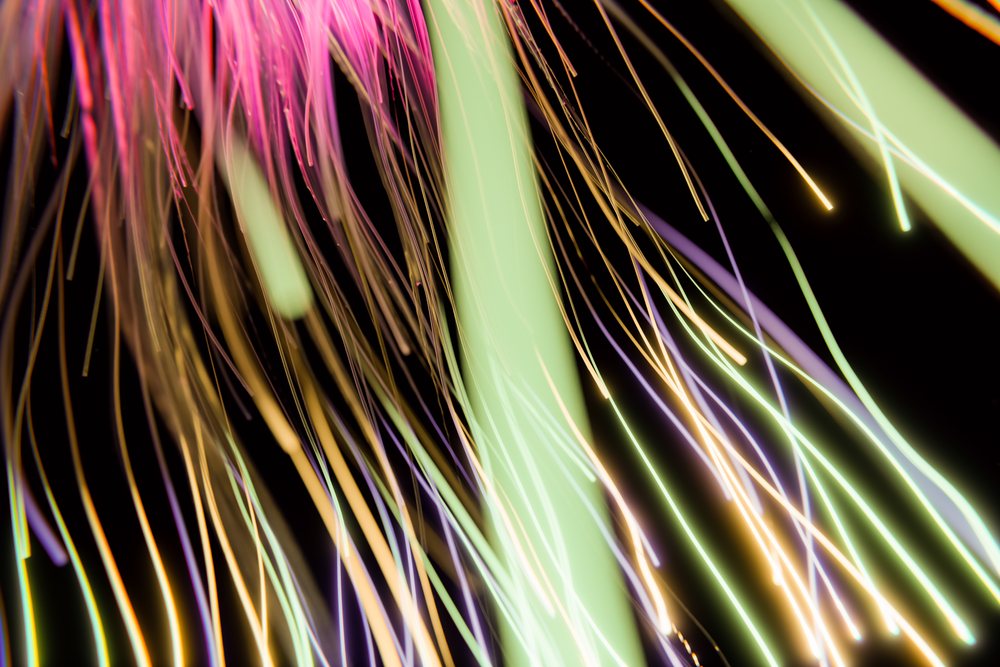 Colorful abstract light streaks in pink, green, yellow, and purple on a black background with flowing motion effect.