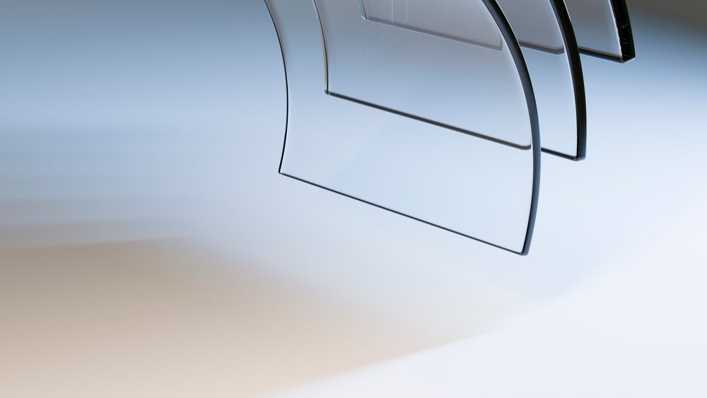 Stack of clear curved glass sheets with smooth edges and reflective surfaces on a white background.