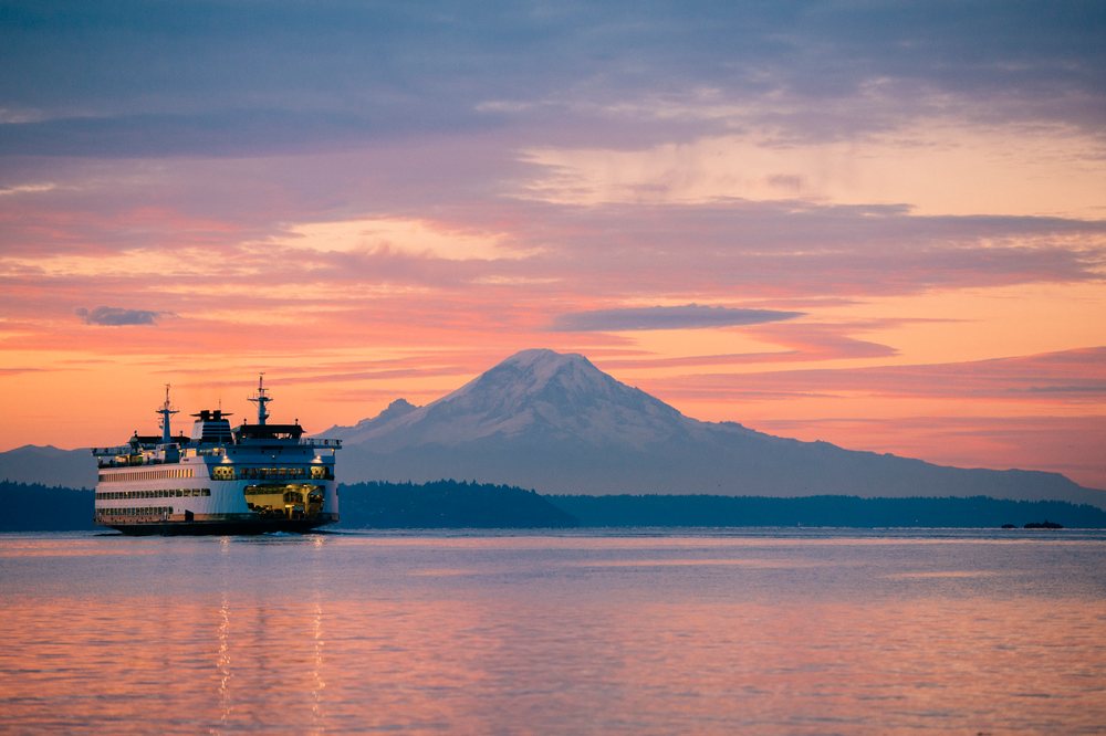 Ferry sails on calm water with Mount Rainier visible at sunset and clouds reflected in the ter, Bainbridge Island, WA, USA.
