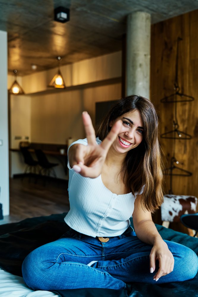 Young woman smiling and showing peace sign while sitting indoors