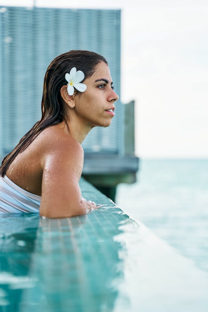 A white woman relaxes in a pool with ocean view