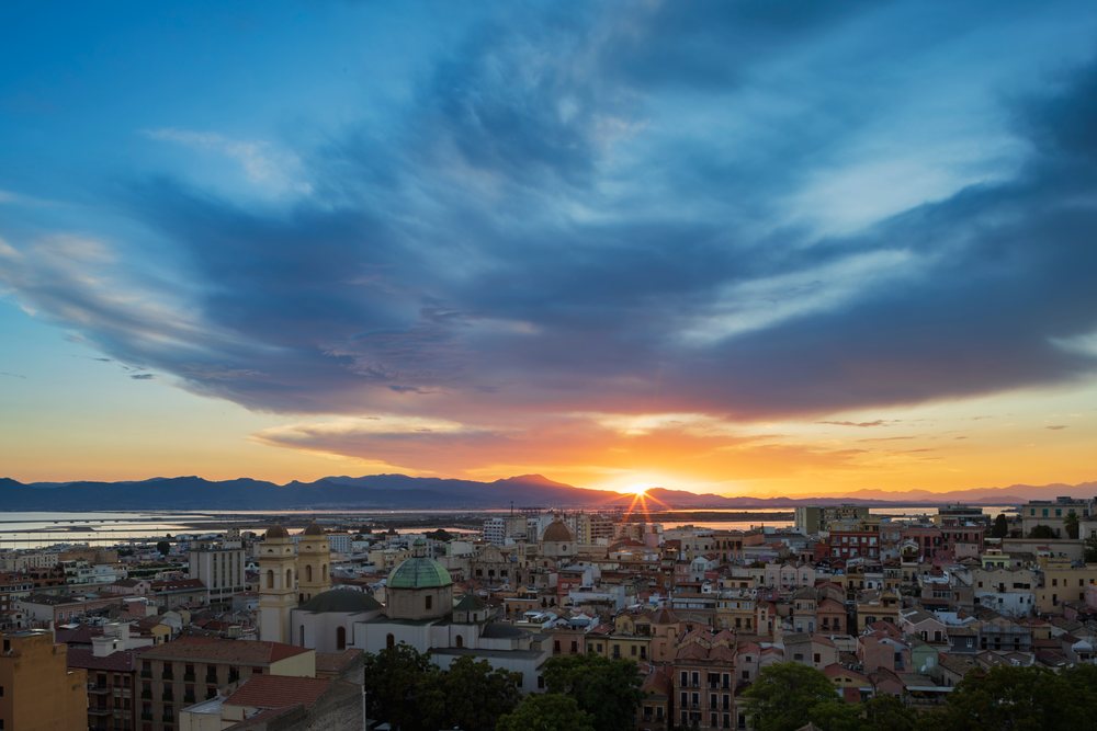 Cagliari city skyline at Sunset with glowing sun and clouds above coastal Sardinia, Travel Photography, Italy.