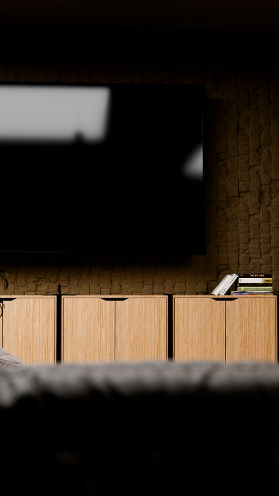 Flat screen television mounted on brick wall above wooden cupboard with books in a modern living room interior.