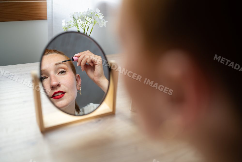 A white woman applies mascara looking