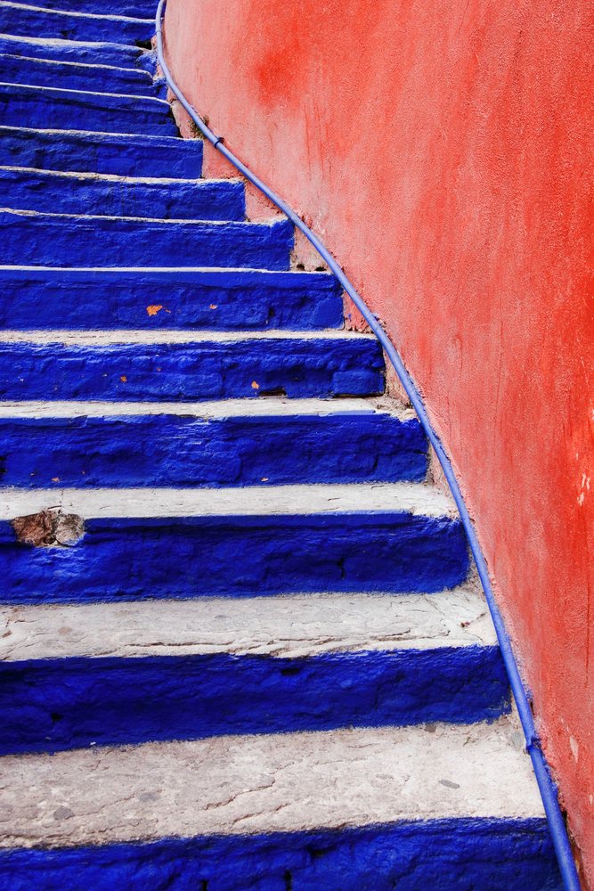 Stone steps painted blue beside an orange textured wall with a curved handrail, Guanajuato, Mexico.