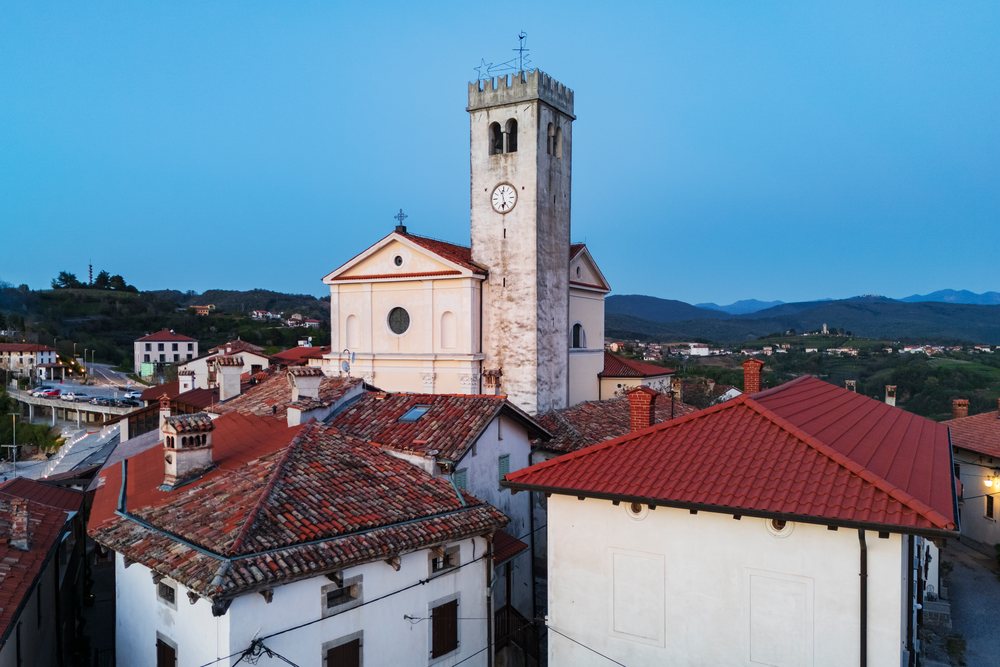 Parish Church of St. Martin with clock tower overlooking red tile roofs and mountains at Dusk, Vipava Valley, landscape, cityscape, Šmartno, Slovenia.