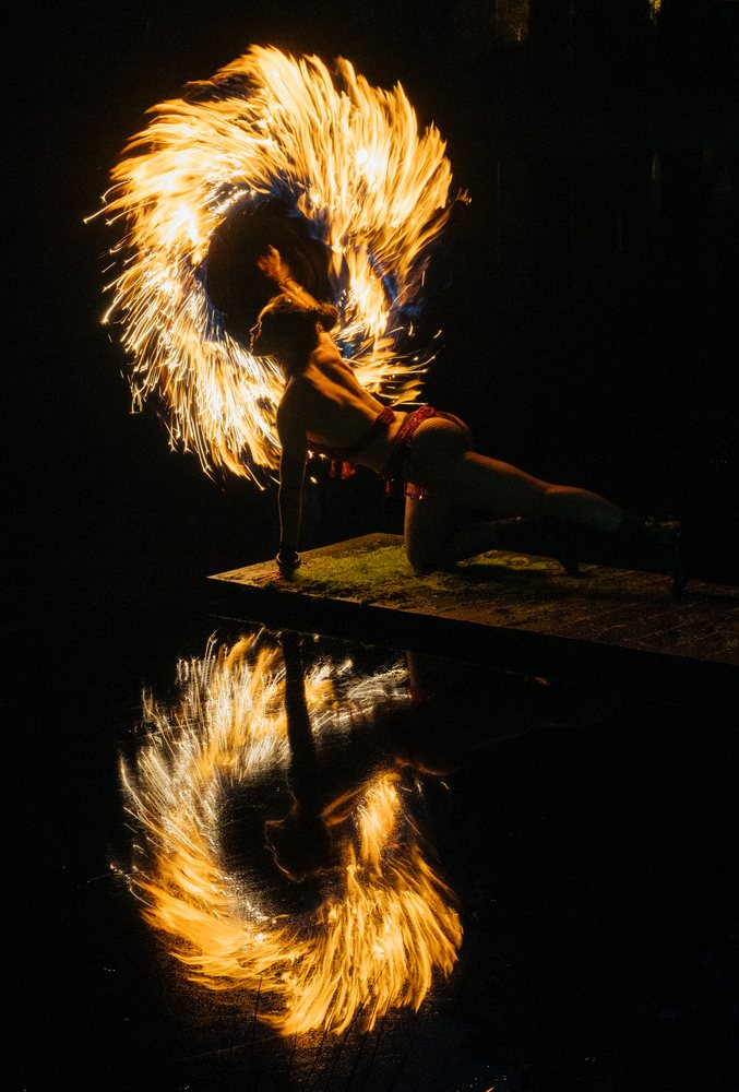 Fire performer spins flaming fire at night with their reflection visible in water, artistry, artist, USA.