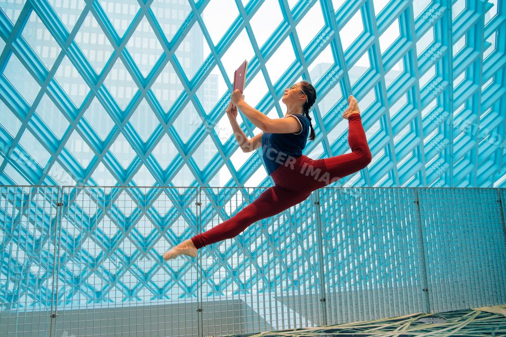 Woman performing ballet leap while reading a book in a library