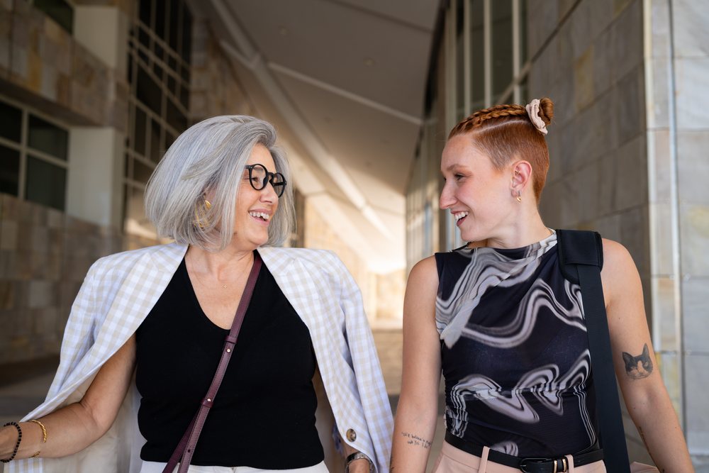 Two businesswomen smiling and talking while walking outside a modern urban building, Spain.