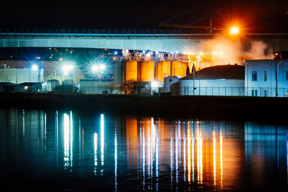 Industrial plant with illuminated storage tanks and bright lights reflecting on water at night, Tacoma, WA, USA.