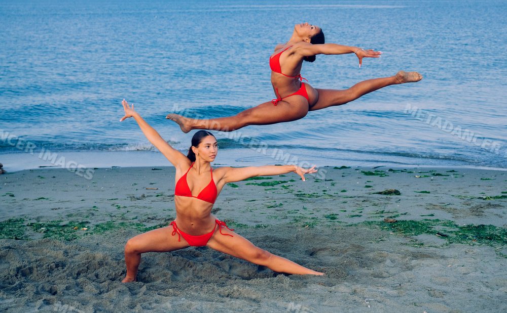 Two women perform partner acrobatics yoga on a sandy beach in WA, USA