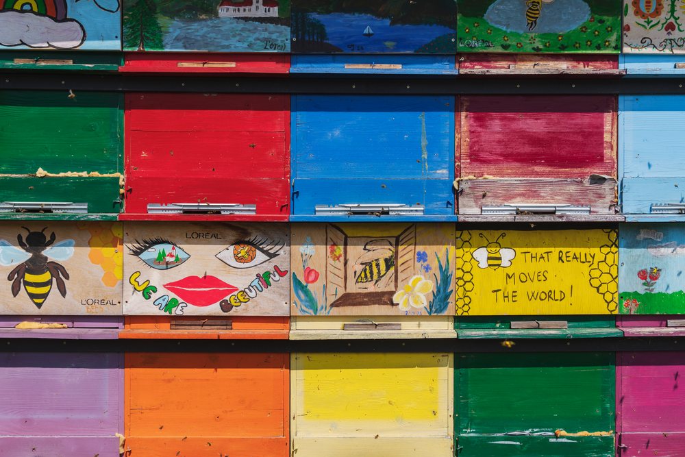 Colorful wooden bee hives with decorative paintings and bees flying around in an outdoor apiary, Landscape, Bled, Slovenia.