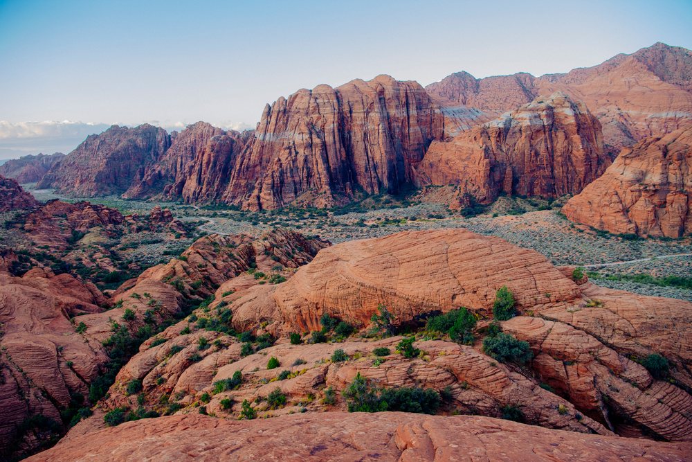 Red Cliffs Desert landscape featuring red sandstone rock formations and green valley vegetation under a clear blue sky, Snow Canyon, Utah, USA.