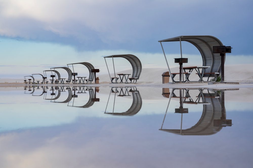 Multiple cabanas with picnic tables, barbecue grills, and trash bins reflect in a flooded area at white Sands National Monument, Landscape, Wildlife, Alamogordo, New Mexico, USA.