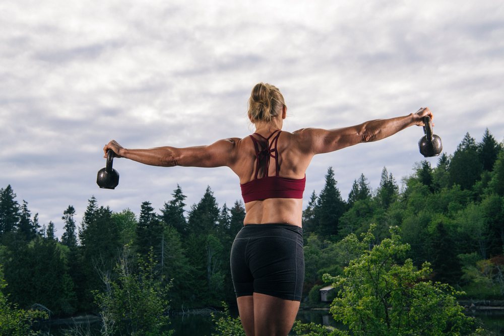 Woman exercising with kettlebells outdoors by a lake, USA.
