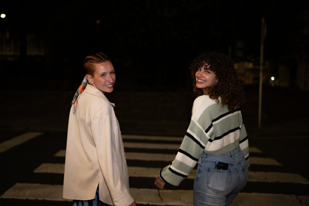 Two women smiling and holding hands while walking together across a crosswalk at night, friendship, Santiago De Compostela, Spain.