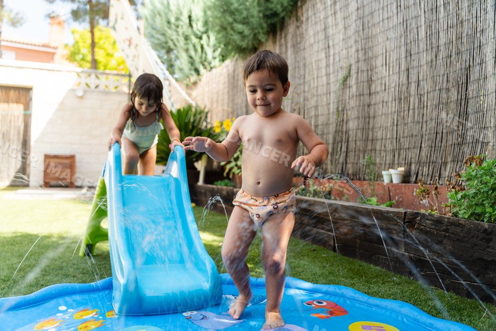 White Children playing on a water slide in a sunny backyard