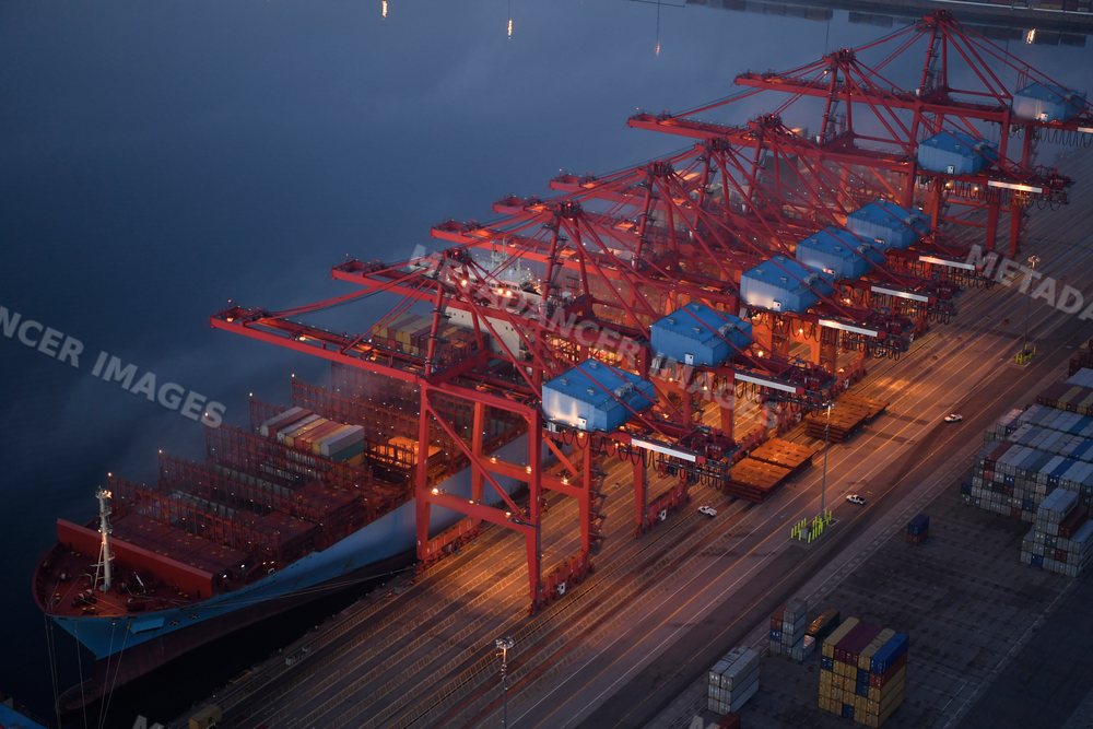 A container ship is loaded with cargo containers at port cranes