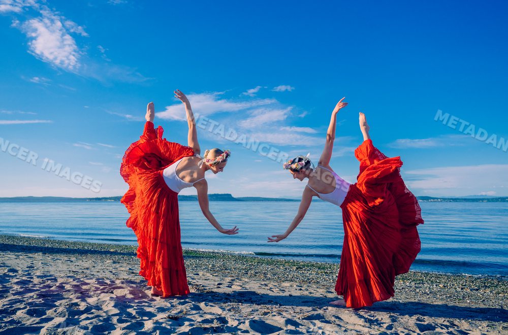 Two white women perform partner yoga acrobatics on a sandy beach