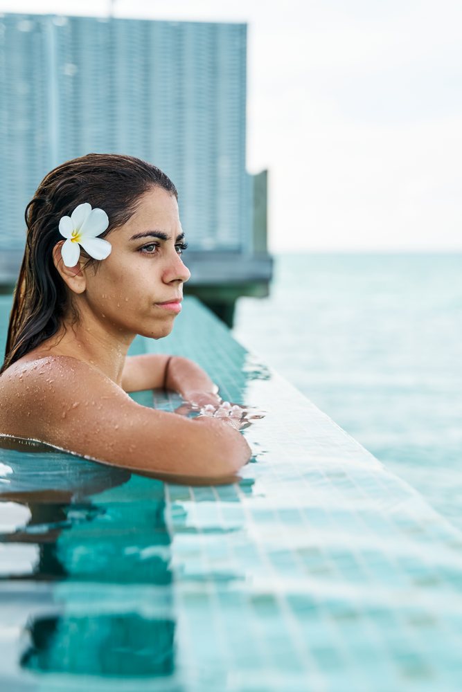 A white woman relaxing in an infinity pool at a resort