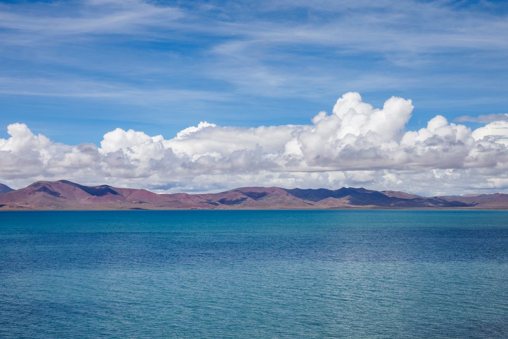 Lake Cuona shows blue water beneath white clouds and distant mountains in Kham Tibet, Amdo County, Autonomous Region of Tibet.