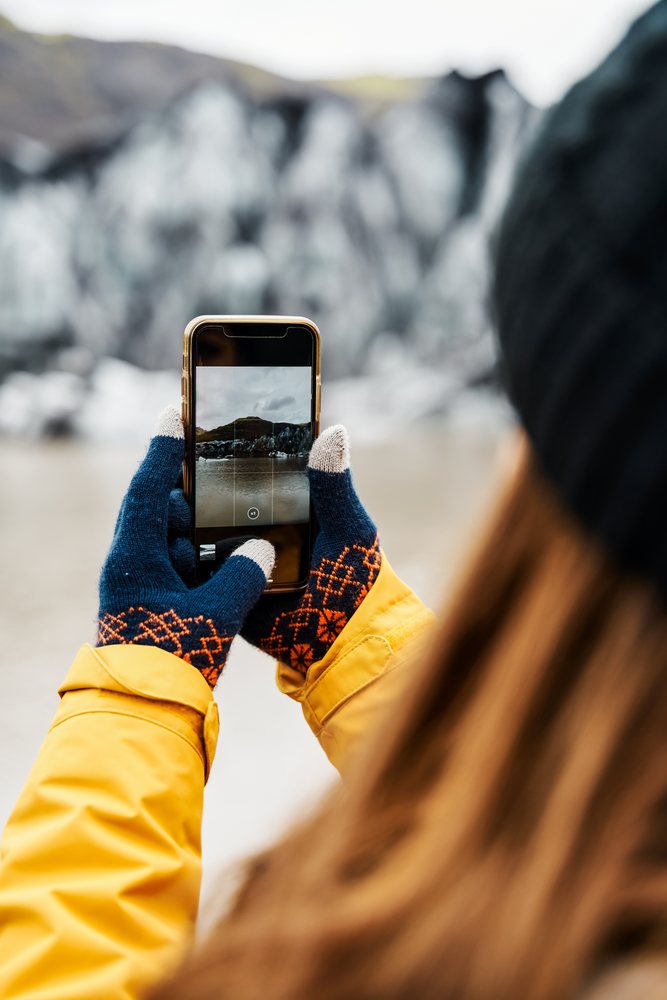 A white person captures a photo of a glacier