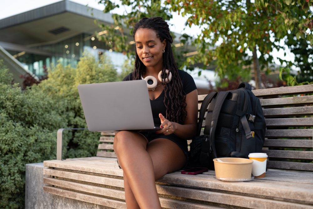 A woman works on her laptop while sitting on a bench in an urban outdoor setting, Santiago De Compostela, Spain.