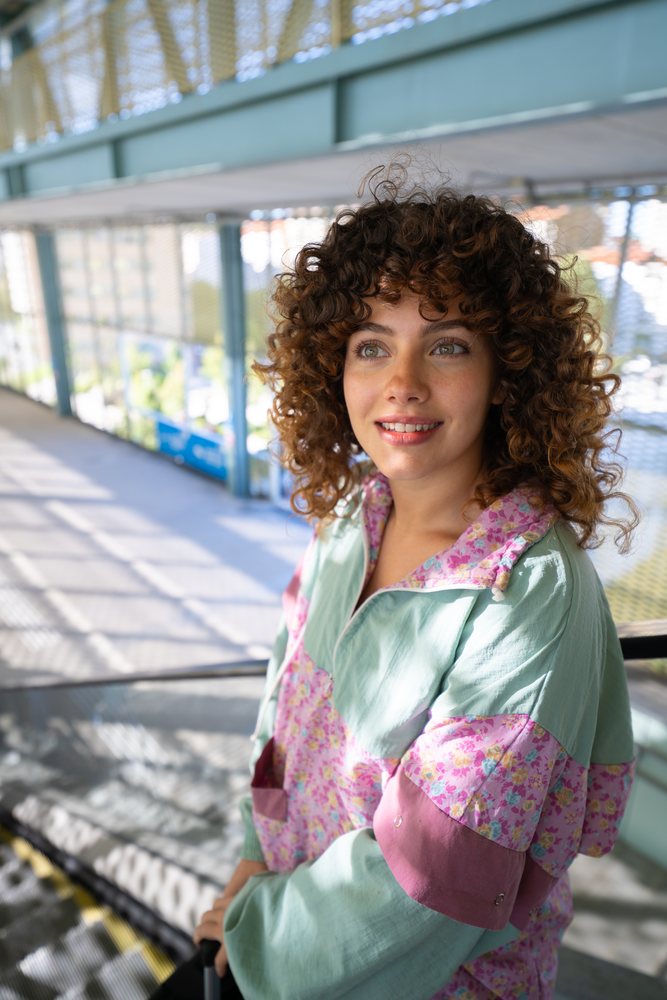 Woman with curly hair smiling on an escalator in an urban setting during daylight, Spain.