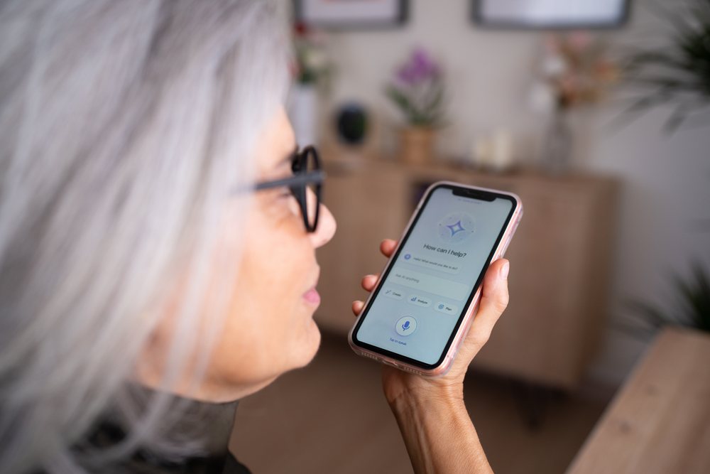 Woman with gray hair uses a voice assistant on her smartphone indoors in a modern home environment, Spain.