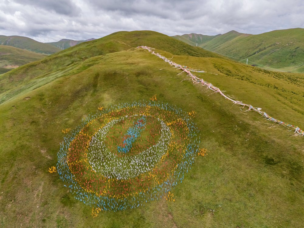 Aerial view shows colorful Prayer Flags forming a symbolic pattern on a green hill near Zhujiesi Monastery in Kham Tibet, Zhenqinzhen, Qinghai Province, Anduo Tibet.