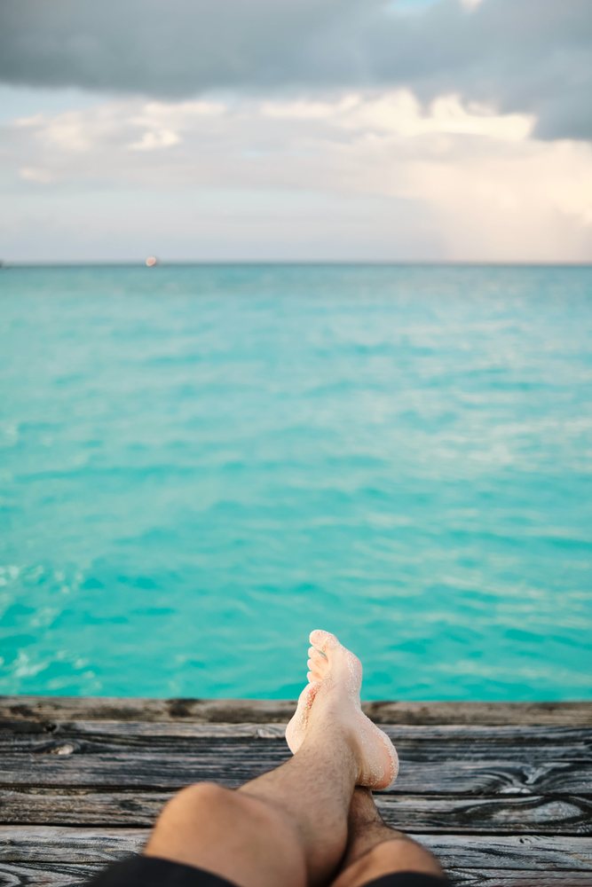A person relaxes with sandy feet on a dock overlooking the turquoise