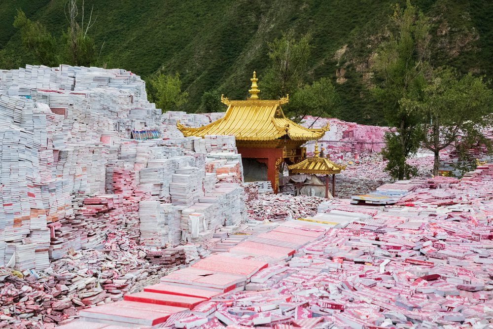 Mani Wall of stacked prayer stones surrounds golden roofed temple structures amid greenery and mountains, Xinzhai, Qinghai Province, People's Republic of China.