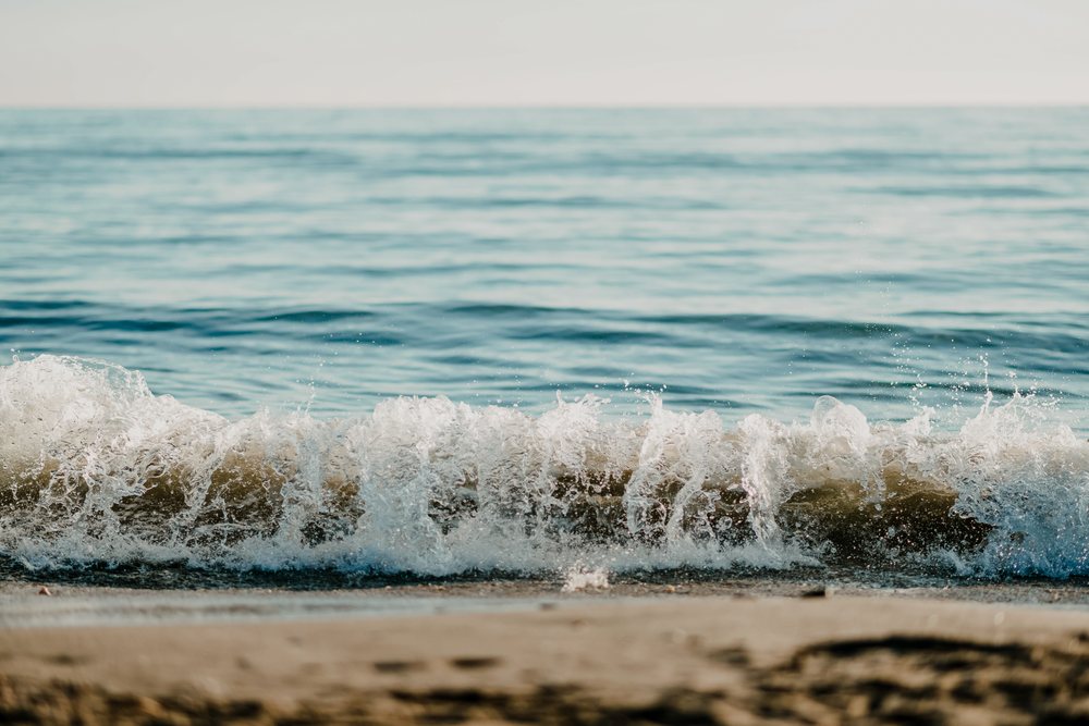 Ocean wave breaking with white sea foam on a sandy beach under a clear sky, Spain.