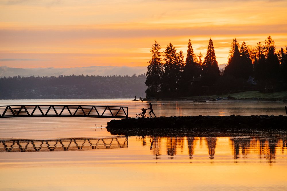 Silhouette of a woman pushing a stroller on a rocky pier at sunset over a calm lake, Bainbridge Island, WA, USA.