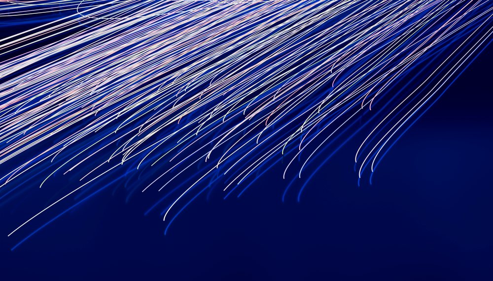 Fiber optic cables illuminated by blue and white light streaks on a dark background, illustrating digital data transmission technology.