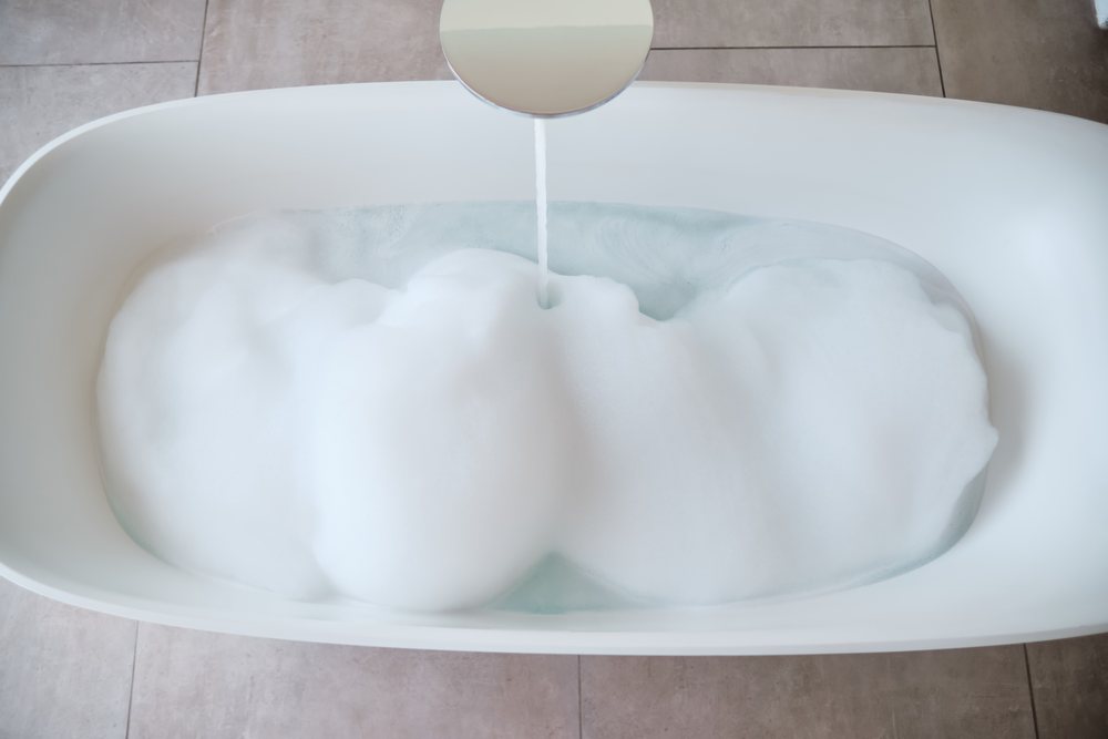 A bathtub is being filled with soapy foam and water in a modern bathroom, Maldives.
