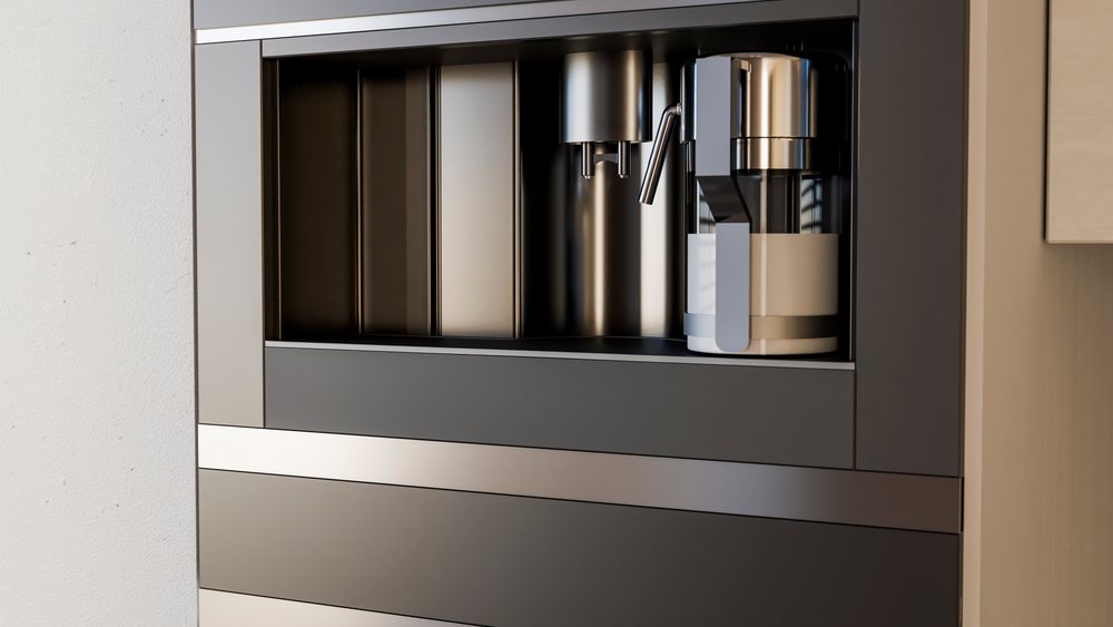 Built-in coffee machine with a coffee pot inside integrated into stainless steel and black modern kitchen cabinetry.