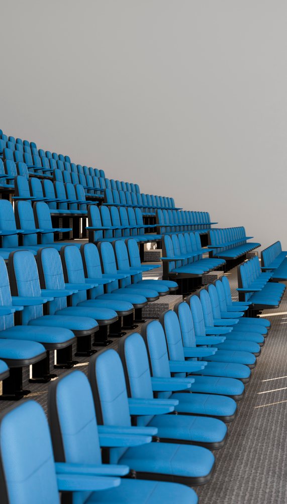 Tiered rows of blue upholstered seats with armrests in an empty modern conference hall.