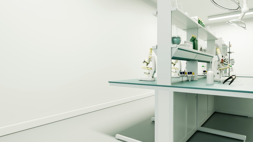 Laboratory microscopes, glass bottles, flasks, test tubes, and safety glasses arranged on a white lab bench in a sterile research facility.