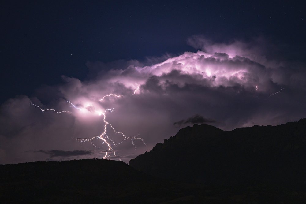 Lightning strikes illuminate storm clouds above a mountain silhouette at night, Travel Photography, Ortgosolo, Sardinia, Italy.