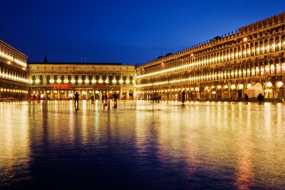 St Mark's Square, illuminated at night with people walking and reflections on the wet ground, Venice, Italy.