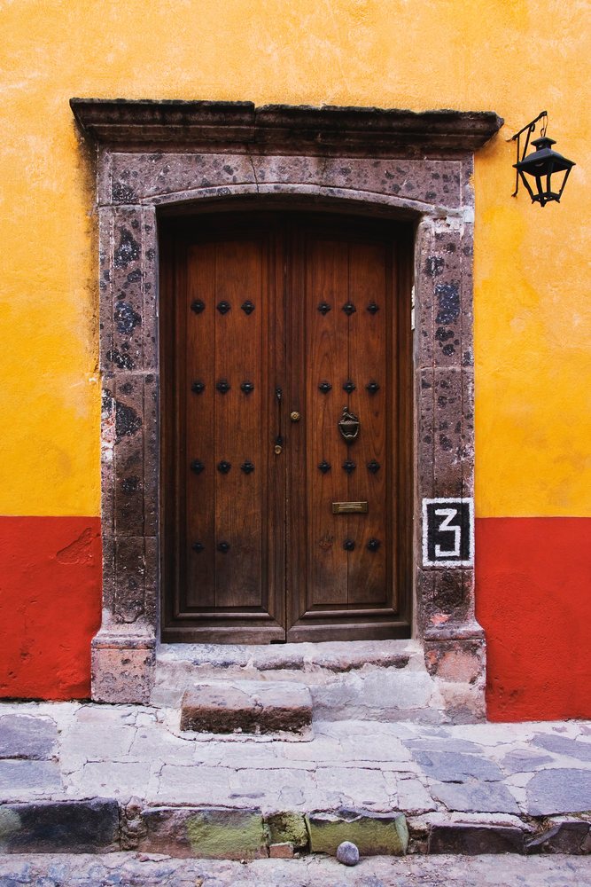 Wooden double door with metal decorations set in a stone doorway on a yellow and red wall, Guanajuato, Mexico.
