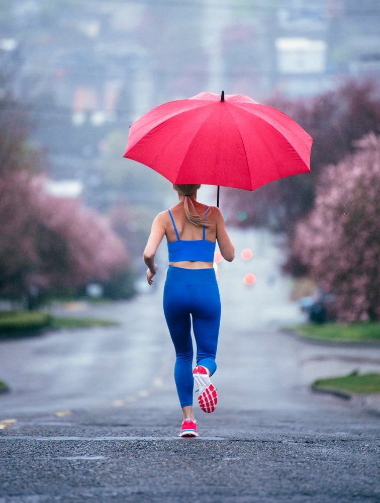 Woman running on a wet urban street holding a red umbrella during rainy weather, USA.
