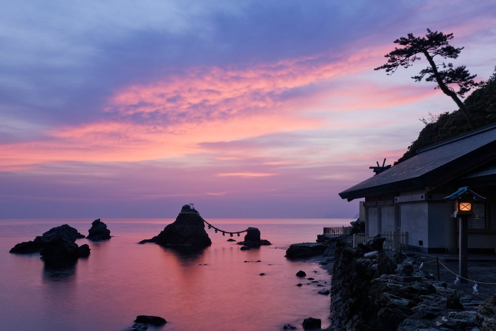 Meoto Iwa rocks connected by a sacred rope beside a Shinto shrine at sunset in Watarai District, Kansai, Honshu, Japan.