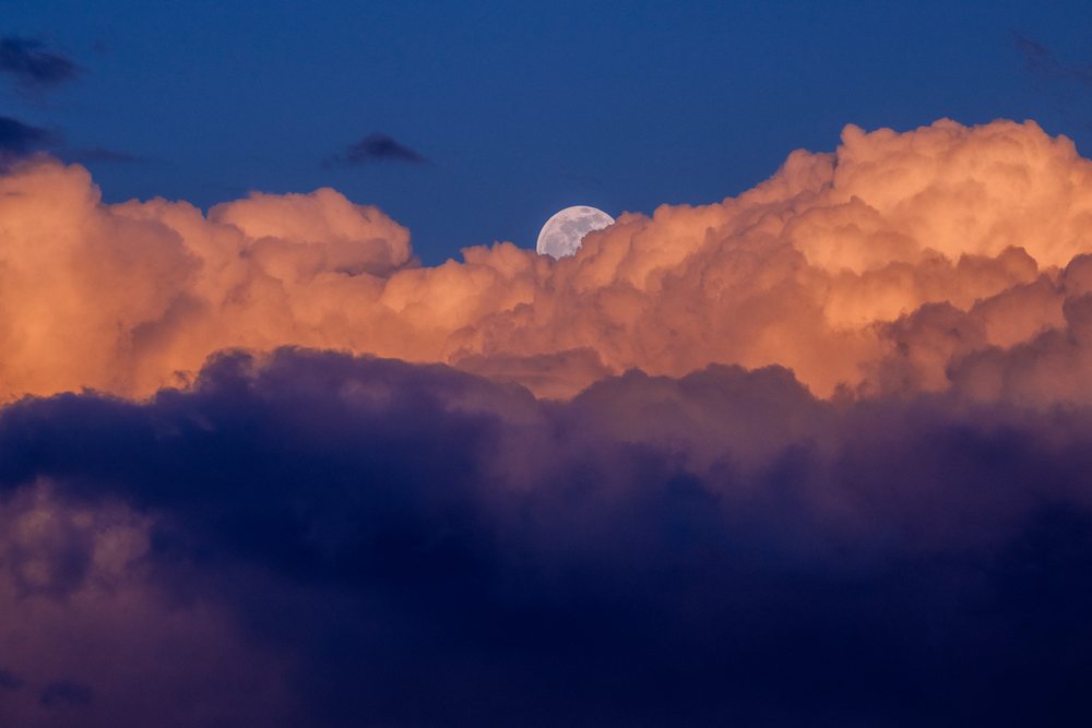 Moon rising above vibrant orange and dark blue clouds at twilight, Seattle, USA.