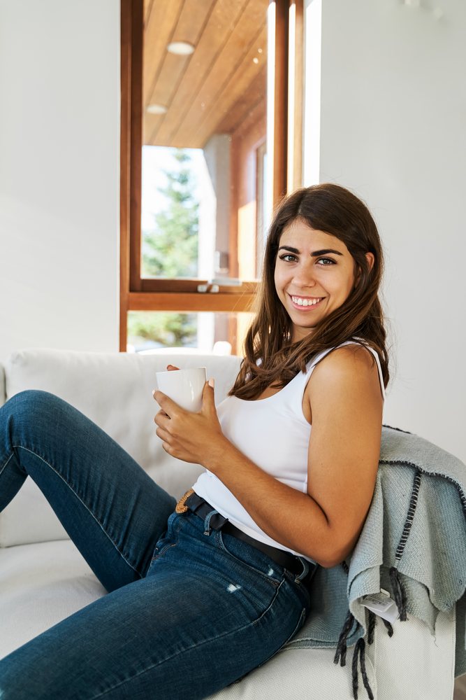 Young white woman relaxing on a couch with a mug in a bright room