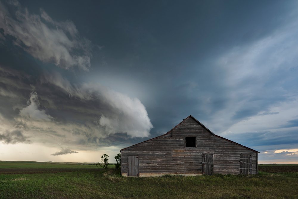 Old wooden barn stands in a grassy field under dark Storm Clouds, Storm Chasing, Weather, Environmental, Wood, South Dakota, USA.