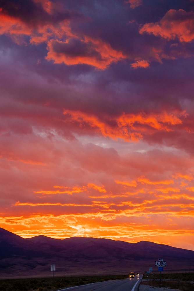 Sunset illuminates the Nevada mountains and highway with vibrant colorful clouds and vehicles on the road, USA.